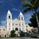 A church building with two steeples with a group of tourists in the courtyard